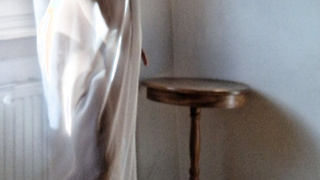 Frau am Fenster in Gardine gehüllt