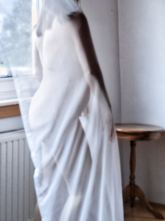 Frau am Fenster in Gardine gehüllt